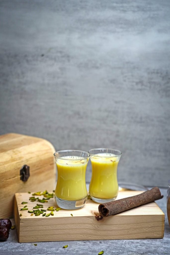 Two glasses of turmeric milk with spices on a rustic wooden table setting.