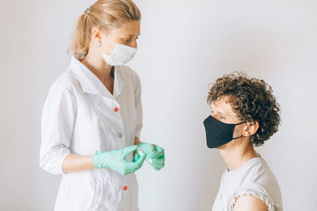 A nurse wearing a mask prepares a vaccine for a masked patient indoors, promoting health care.